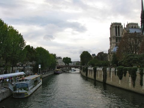 The Seine curves past moored barges and leafy banks, the towers of Notre-Dame standing on the right under a soft grey sky.