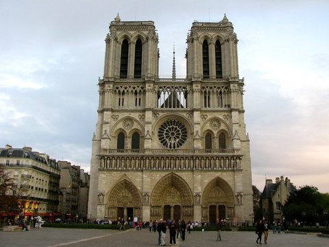 The twin towers and rose window of Notre-Dame rise above its three sculpted portals, small figures crossing the square at dusk.