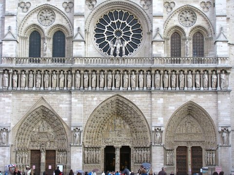 Close view of the three carved portals, the row of kings and the rose window of Notre-Dame, with umbrellas dotting the pavement below.