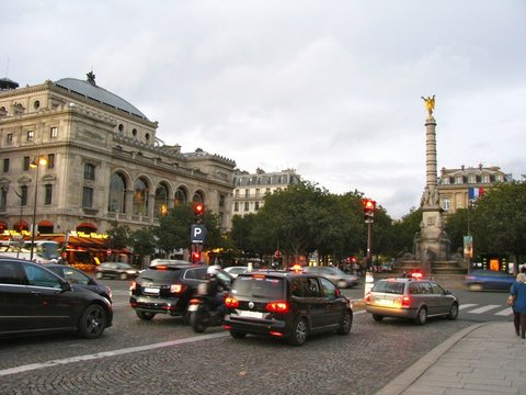 Evening traffic circles the gilded column of the Fontaine du Palmier, with the domed Théâtre du Châtelet and glowing cafe awnings to the left.