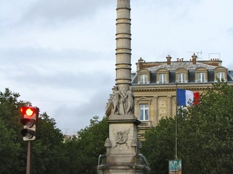 A gilded winged Victory tops the tall banded column of the Fontaine du Palmier, sphinxes at its base and a French flag on the building behind.