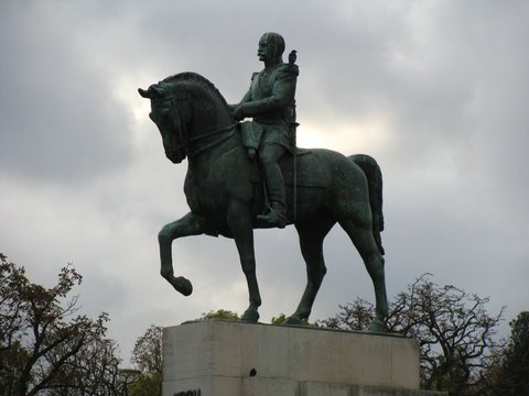 Dark bronze of a uniformed officer on a high-stepping horse silhouetted against heavy grey cloud, a small bird perched on his shoulder.