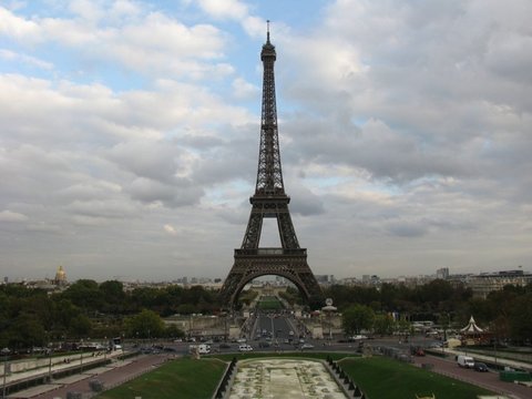 The Eiffel Tower seen head-on across the Trocadéro gardens and the Pont d'Iéna, under a sky of broken grey and white cloud.