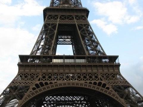 Looking up at the first and second levels of the Eiffel Tower, its iron lattice arching over a glimpse of the city beyond.
