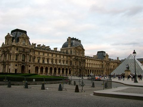 The ornate Louvre facade and domed pavilion under a pale pink-grey sky, the glass pyramid and equestrian statue at the right edge.
