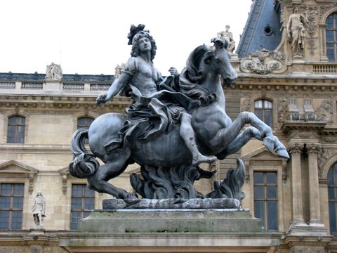 Equestrian statue of a rider on a rearing horse, set on a stone plinth against the carved windows of the Louvre facade.