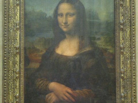 The Mona Lisa behind glass in its carved gilt frame, the sitter's folded hands and faint smile against a hazy blue landscape.