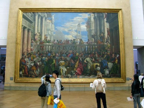 The Wedding at Cana, the Louvre's largest painting, a vast gilt-framed banquet beneath classical columns, visitors small in front of it.