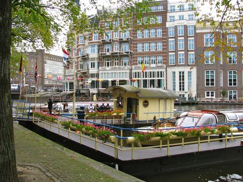 A yellow boat landing lined with pink flower boxes floats before grand canal-side hotels hung with bunting and a row of national flags.