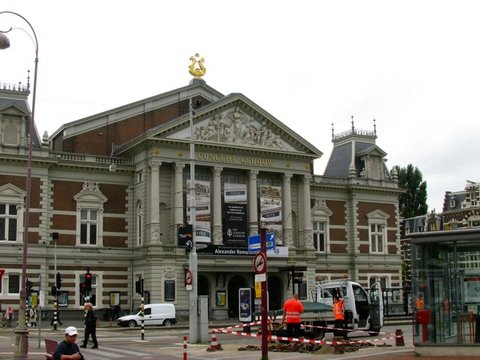The neoclassical Concertgebouw with its gilded lyre and sculpted pediment stands behind traffic lights and roadworks on an overcast day.
