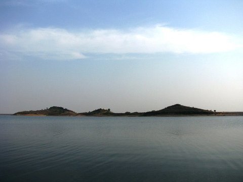 Three low rounded islands sit along the horizon beyond a stretch of gently rippled grey-blue water under a pale sky.