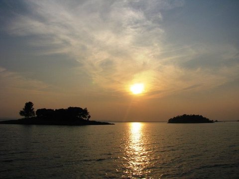 The sun sinks between two dark wooded islands, streaking the water with gold beneath a sky of wispy cirrus.