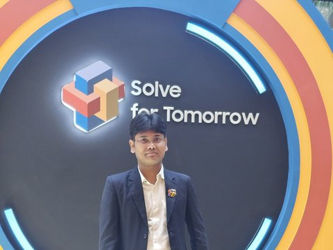 Dr. Pinaki Bhaskar in a dark suit on the lit podium in front of the circular Solve for Tomorrow backdrop at the Grand Finale.