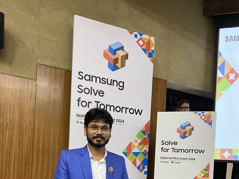 Dr. Pinaki Bhaskar in a blue checked blazer on the auditorium stage beside the Samsung Solve for Tomorrow National Pitch Event 2024 standees at IIT Delhi.