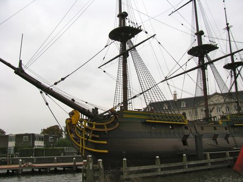 The masts, yards and rigging of a moored three-masted sailing ship against a pale overcast sky.