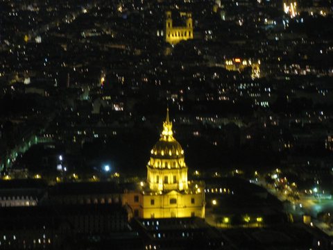 The gilded dome of Les Invalides glowing among the city lights of Paris, seen from above at night.