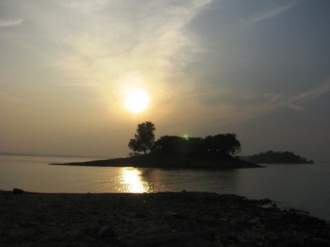 Low sun above a small wooded island, its reflection a bright path across the still reservoir.