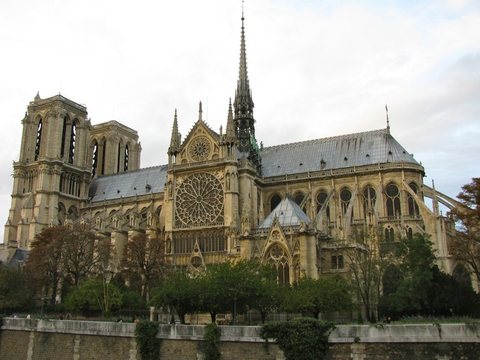 The south side of Notre-Dame cathedral with its spire and rose window, above the trees of the riverbank.