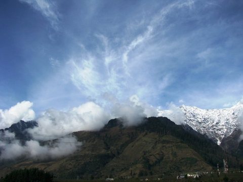 Snow-dusted Himalayan peaks wrapped in cloud beneath a deep blue sky streaked with cirrus.