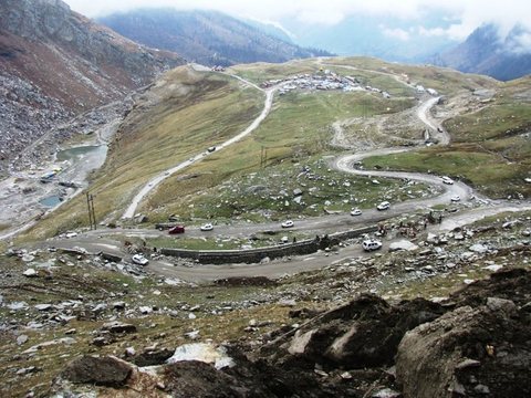 A high green valley crossed by a road of tight switchbacks, with vehicles small in the distance.