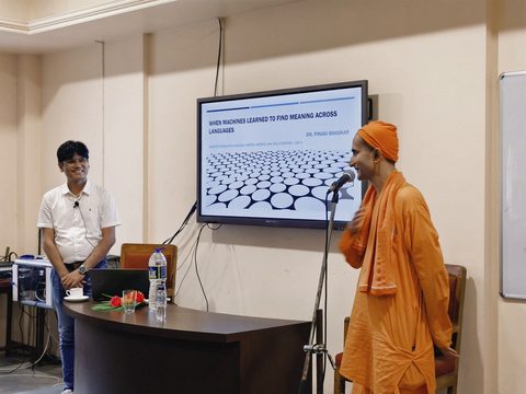 Dr. Pinaki Bhaskar beside a monk of the Ramakrishna Mission addressing the room, next to the title slide “When machines learned to find meaning across languages”.